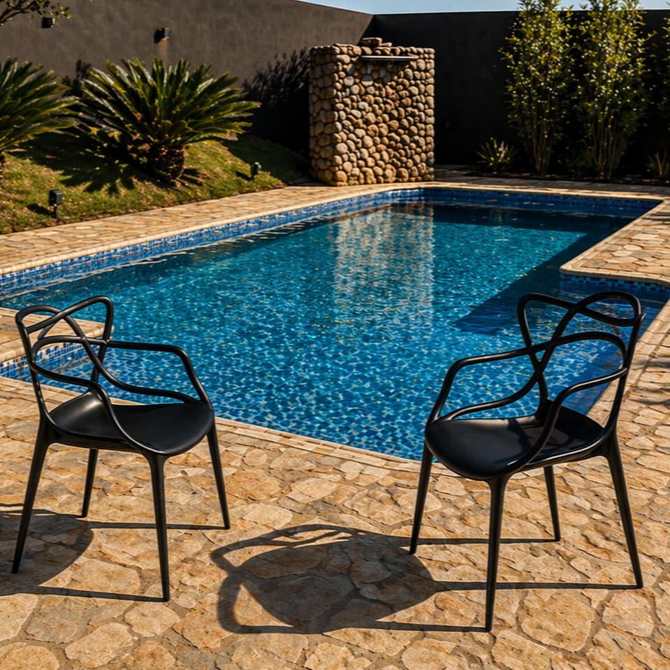 Cadeiras modernas pretas para área de piscina ao lado de uma piscina azul com fundo de pedra e grama verde