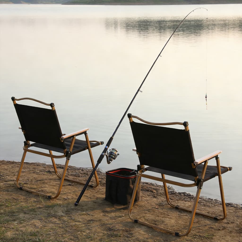 Cadeiras dobráveis pretas na margem de uma lagoa com vara de pesca e recipiente preto