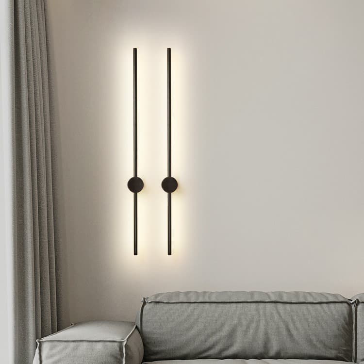 Luminária de parede moderna preta com lâmpadas circulares iluminando uma poltrona cinza.