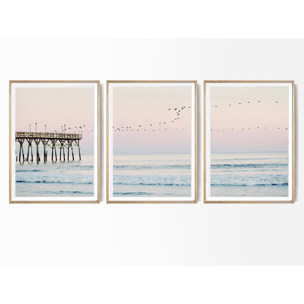 Trêz quadros decorativos de paisagem praial com píer, molduras douradas, tons pastel, pássaros voando.
