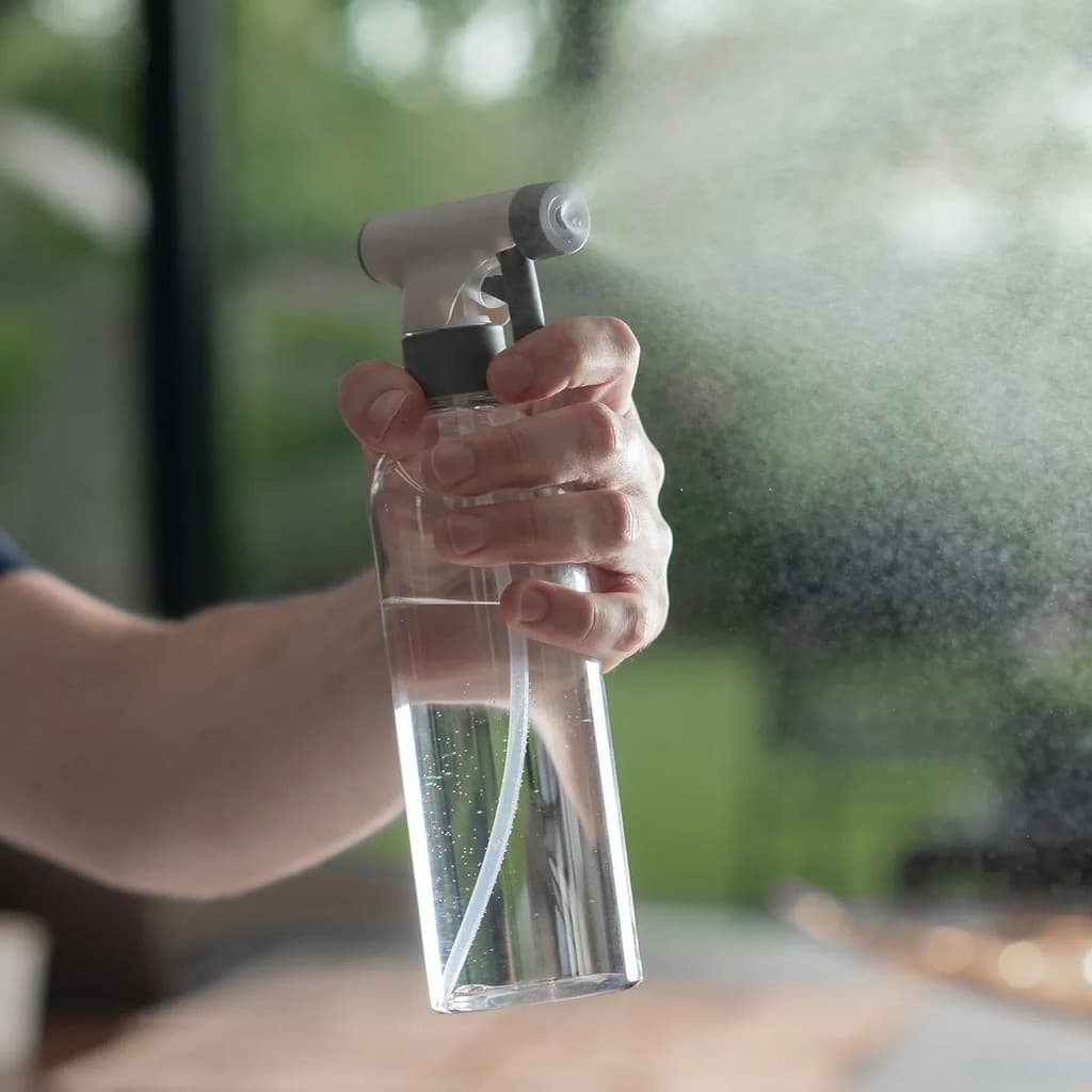 Borrifador multiuso transparente com tampa cinza e preta sendo usado para pulverizar líquido