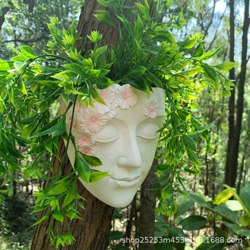 Vaso decorativo de rosto humano com flores rosa e folhas verdes pendurado na parede