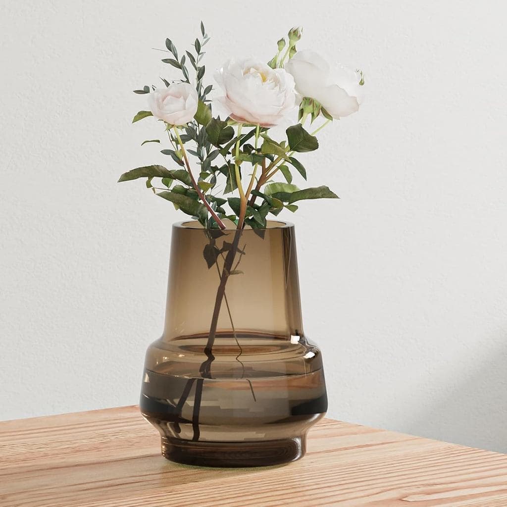 Vaso de vidro âmbar com flores brancas e folhas verdes sobre mesa de madeira