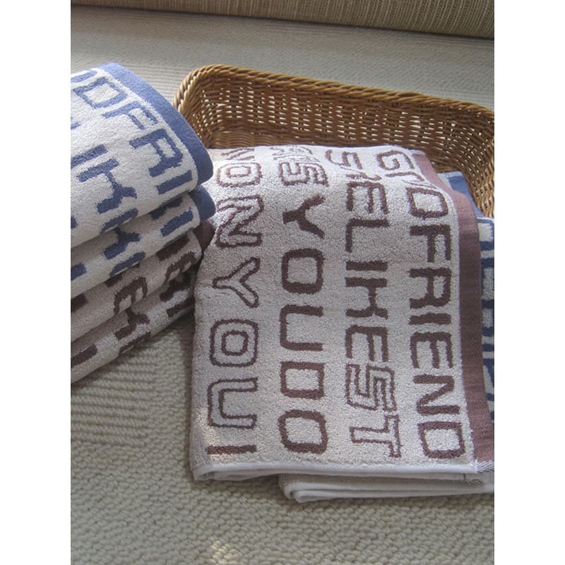 Toalhas de banho em Jacquard com design de texto em relevo, em cores branco, azul e marrom, em um cesto de vime.