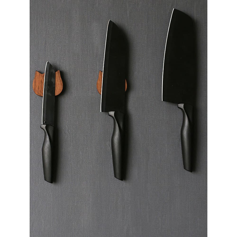 Três facas de cozinha com cabos pretos penduradas em suporte magnético de madeira