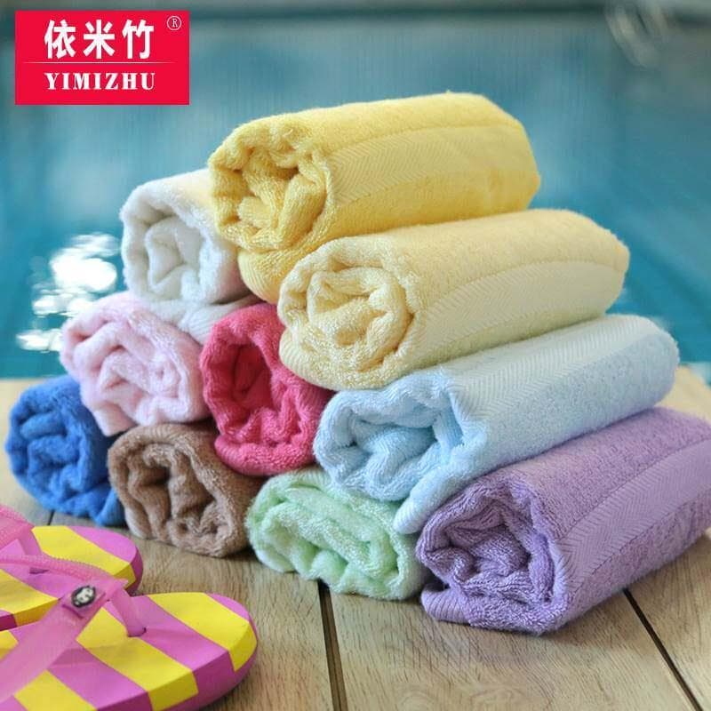 Toalhas de bambu em cores pastel em uma pilha sobre uma superfície de madeira com um chinelo de dedo rosa e amarelo ao fundo