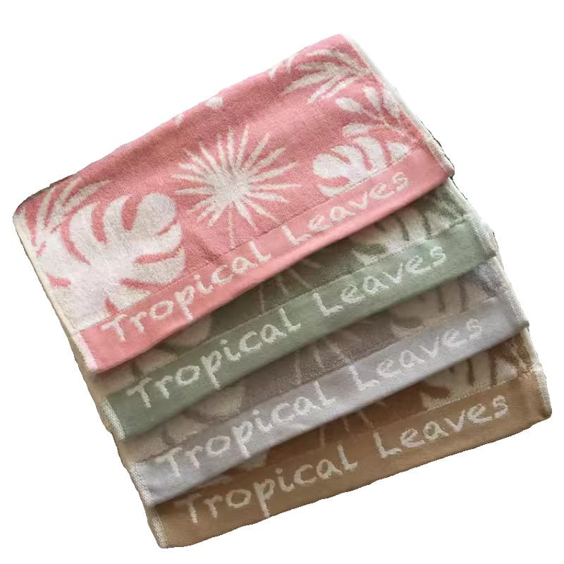 Toalhas de banho Tropica Leaves empilhada em cores rosa, verde e marrom com padrão de folhas tropicais