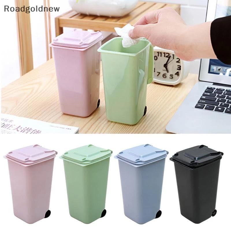Mini lixeiras de mesa com tampa de lixo, cores rosa, verde, cinza, azul e preto, mesa de madeira, relógio e laptop no fundo