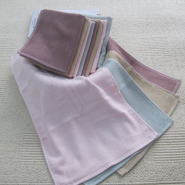 Conjunto de toalhas de fibra de bambu em várias cores, rosa, azul, bege e cinza, sobre uma superfície texturizada.