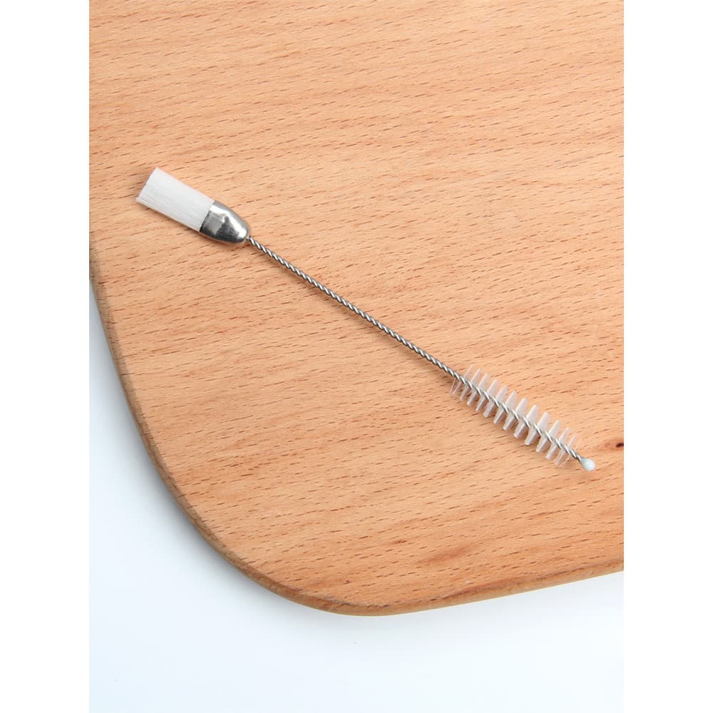 Escova de limpeza de bico de decoração de duas extremidades com cabo metálico e cerdas brancas sobre fundo de madeira.