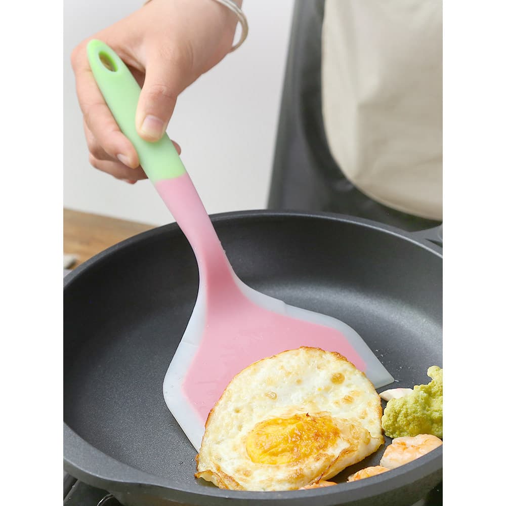 Espátula antiaderente de silicone rosa e verde virando ovo frito em frigideira