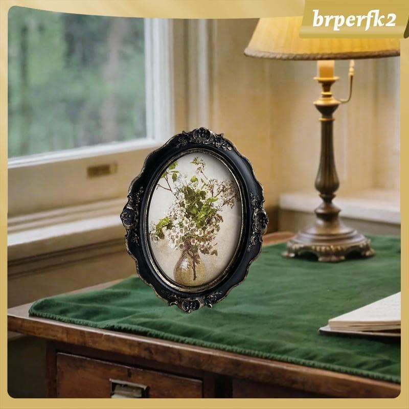 Porta-retratos estilo barroco em resina com flores brancas, sobre mesa com tecido verde escuro, luminária de mesa à direita.