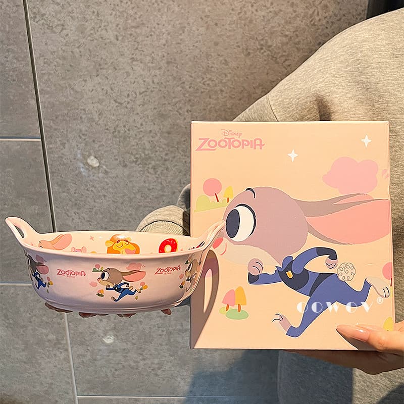 Tigela de cerâmica rosa com desenhos de personagens da Disney ao lado de uma caixa de embalagem com o mesmo tema.