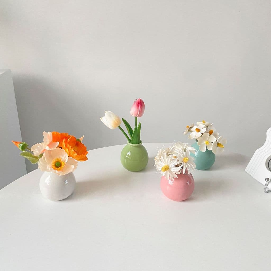 Vasos de cerâmica com flores artificiais em cores pastel em uma mesa branca