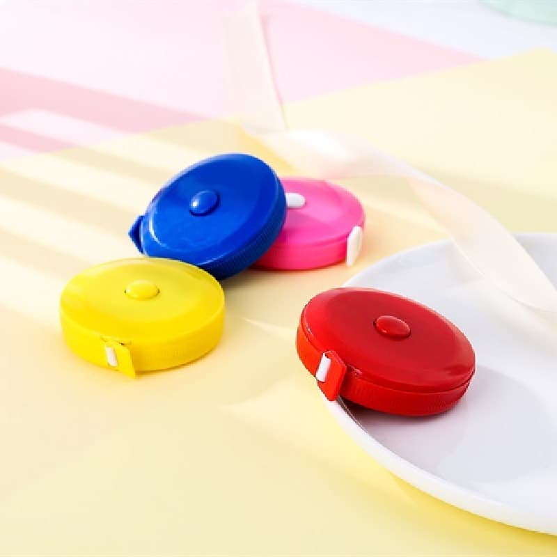 Fitas métricas retráteis coloridas em azul, rosa, amarelo e vermelho sobre fundo branco e amarelo