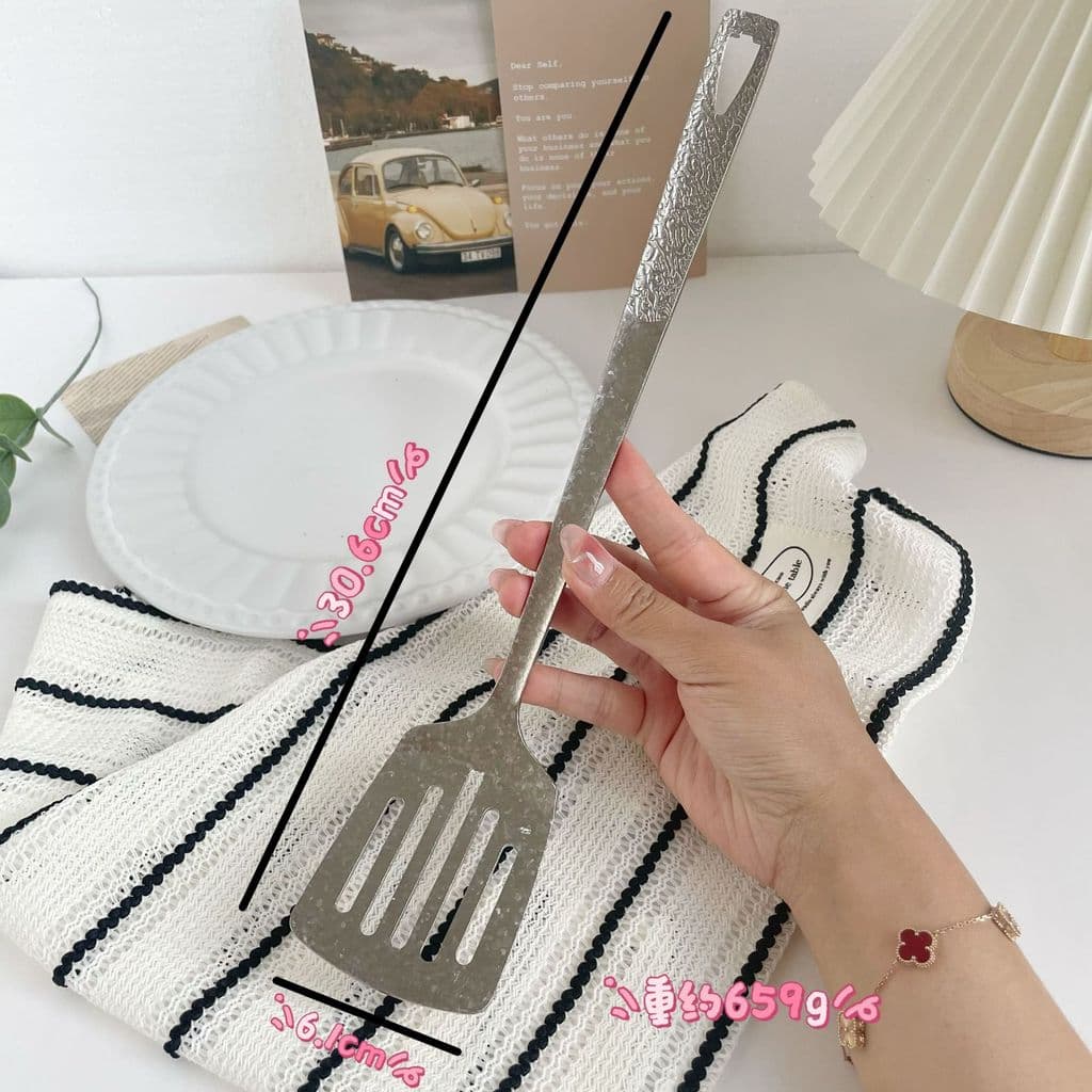 Espátula de titânio puro em mão, com fundo de mesa e toalha listrada