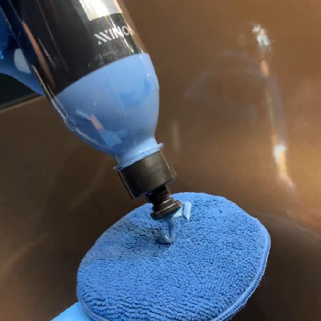 Aplicador de Microfibra Vonixx azul em uso, dispensando produto de limpeza em superfície lisa.