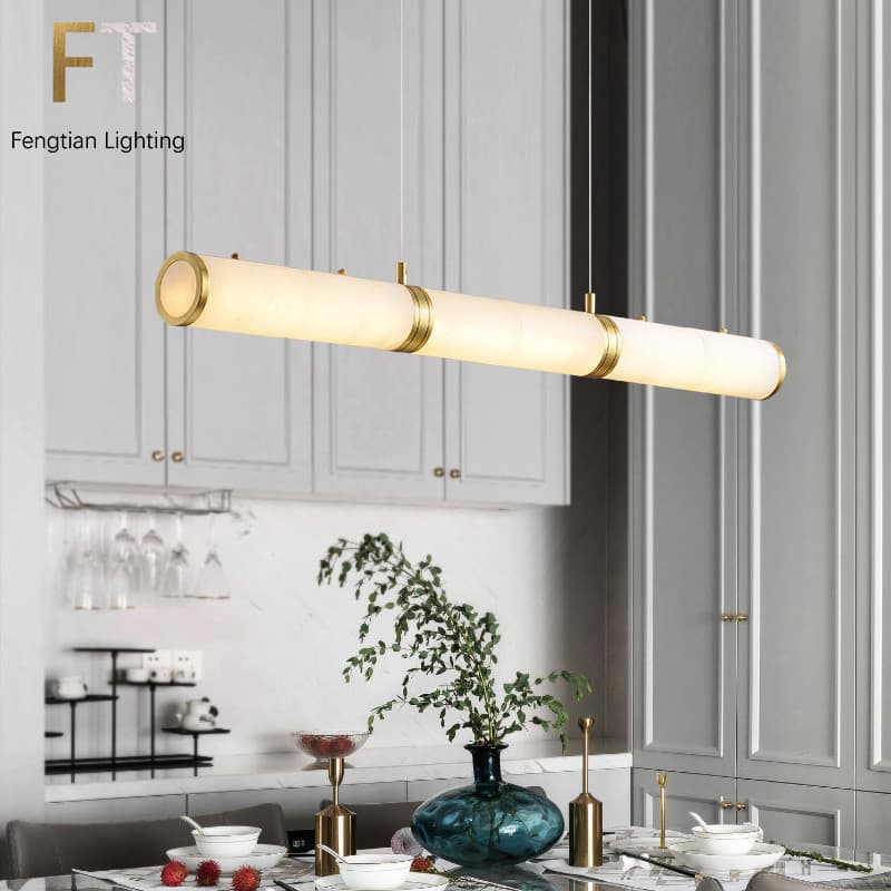 Luminária pendente LED linear em alabastro branco com detalhes dourados, iluminando uma cozinha moderna
