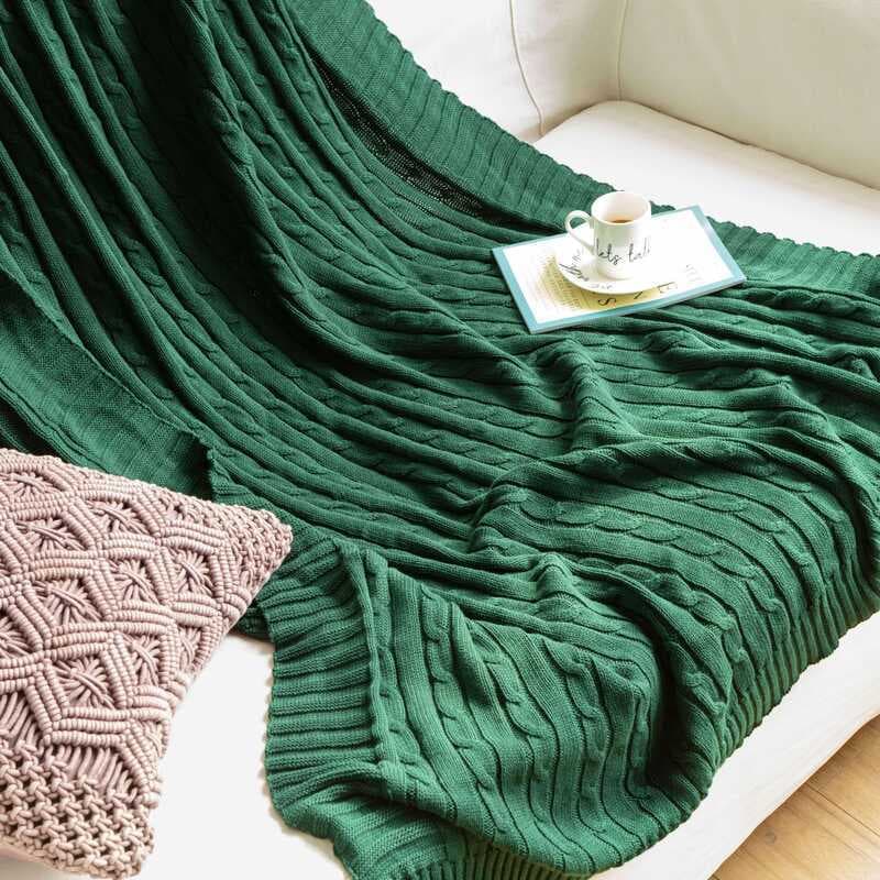 Cobertor de malha nórdico torcido verde escuro sobre sofá branco com xícara e travesseiro decorativo rosa