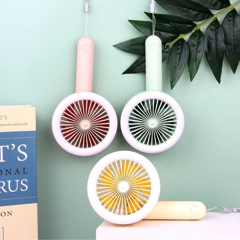 Três ventiladores pequenos dobráveis LED com pás vermelhas, pretas e amarelas, pendurados em uma parede verde.