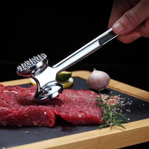 Amaciador de carne de aço inoxidável com alça confortável sobre fatias de carne vermelha.