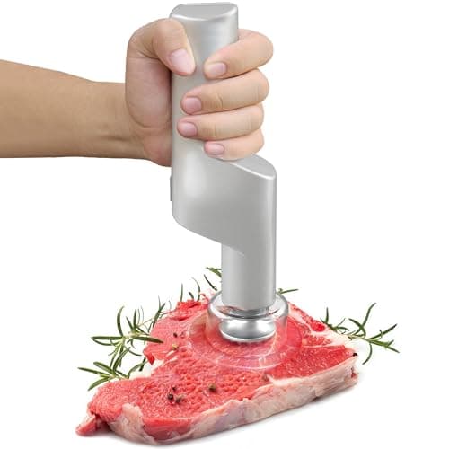 Amaciador elétrico de carne prateado em uso sobre um pedaço de carne vermelha com ervas
