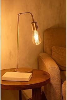 Luminária de mesa industrial dourada em um canto de sala com um livro iluminado