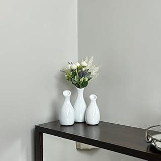 Trio de vasos decorativos brancos com flores em uma mesa marrom