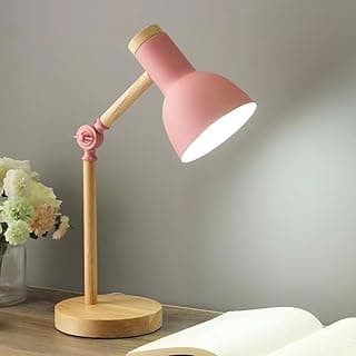 Luminária de mesa rosa com base de madeira, ajustável e compacta, iluminando um ambiente com um livro aberto e flores ao fundo.