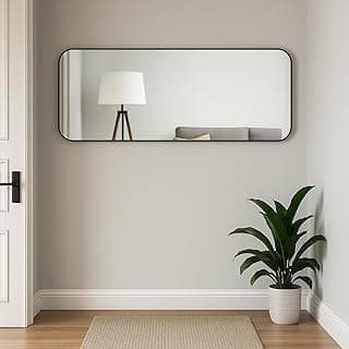 Espelho retangular grande com cantos arredondados, montado na parede, refletindo uma sala com uma lâmpada de pé e uma planta em um vaso branco.
