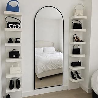Espelho decorativo oval com moldura preta, refletindo uma cama e prateleira com itens, fundo branco.