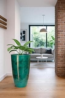 Vaso grande verde marmorizado com planta, sala de estar com sofá cinza e janela.
