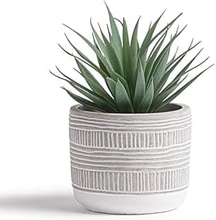 Planta artificial em vaso cinza e branco com listras verticais, folhas verdes pontiagudas, fundo branco