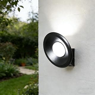 Arandela LED de parede preta iluminando uma parede branca em um jardim