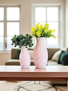 Dois vasos decorativos rosas com plantas e flores sobre mesa de madeira em sala de estar.