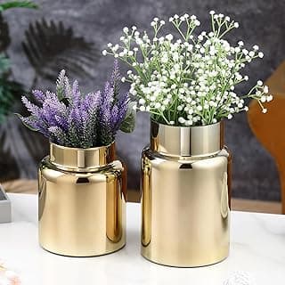 Dois vasos de vidro dourados com flores artificiais em uma mesa branca