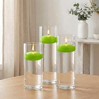 Três velas flutuantes verdes dentro de vasos cilíndricos de vidro transparente sobre uma mesa de madeira