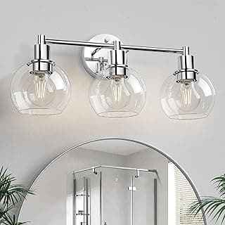 Três luminárias cromadas para banheiro com cúpulas transparentes e globos cromados polidos acima do espelho.