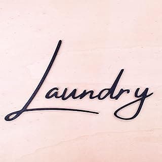 Letreiro decorativo 'Laundry' em preto com efeito 3D sobre fundo rosa claro
