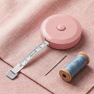 Fita métrica retrátil rosa de 2 m sobre tecido rosa, com agulha e carretel de linha azul