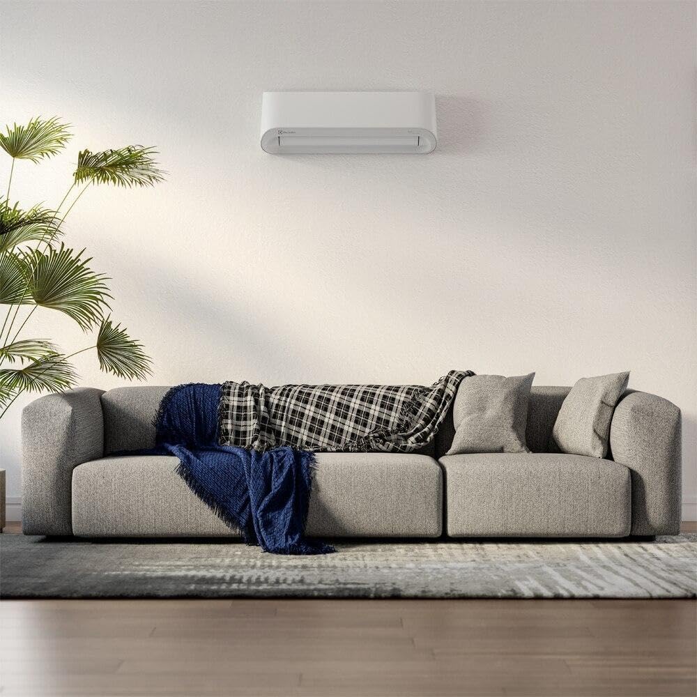 Sala moderna com sofá cinza e ar-condicionado Electrolux Color Adapt Inverter instalado na parede.
