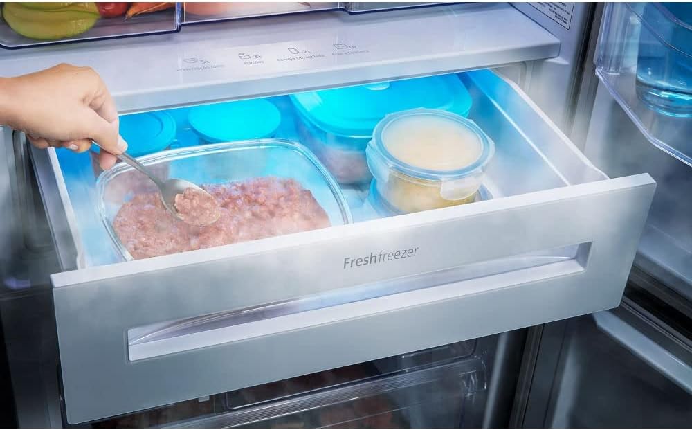 Interior do freezer da geladeira Panasonic mostrando gaveta FreshFreezer com alimentos e mão mexendo na comida