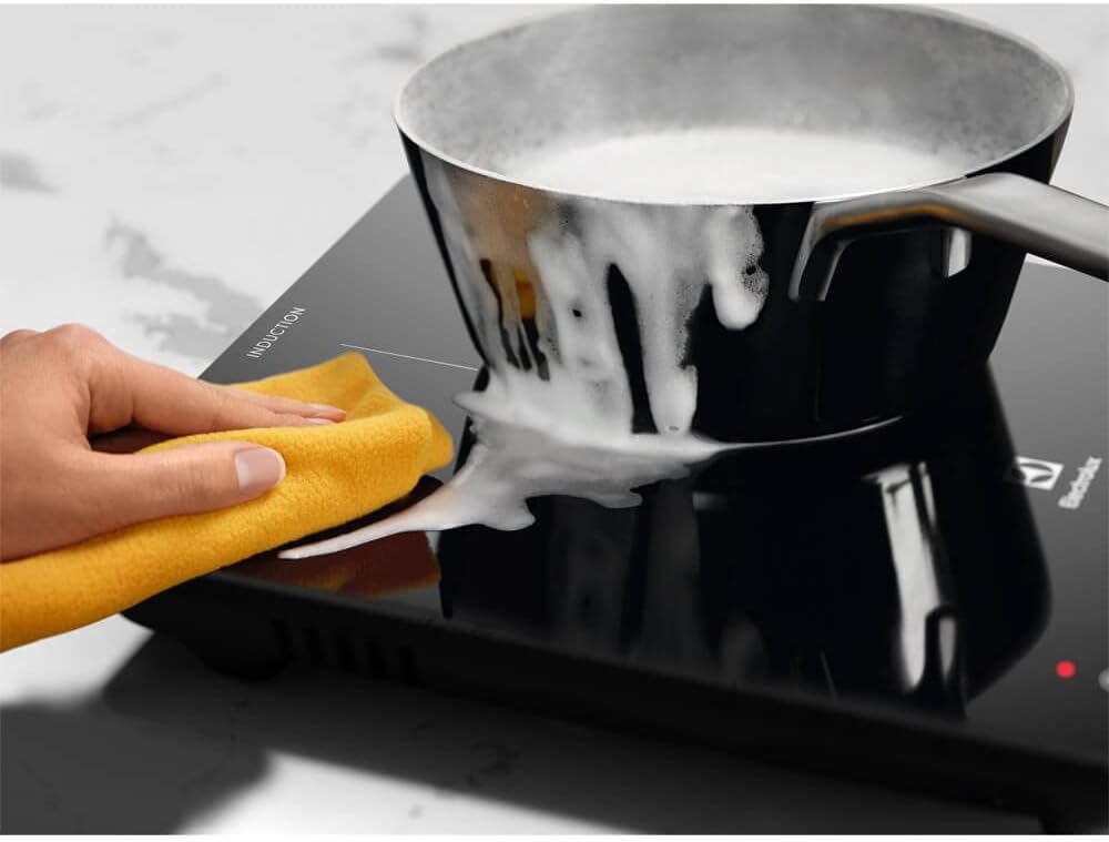 Pessoa limpando cooktop de indução portátil Electrolux preto com pano amarelo.