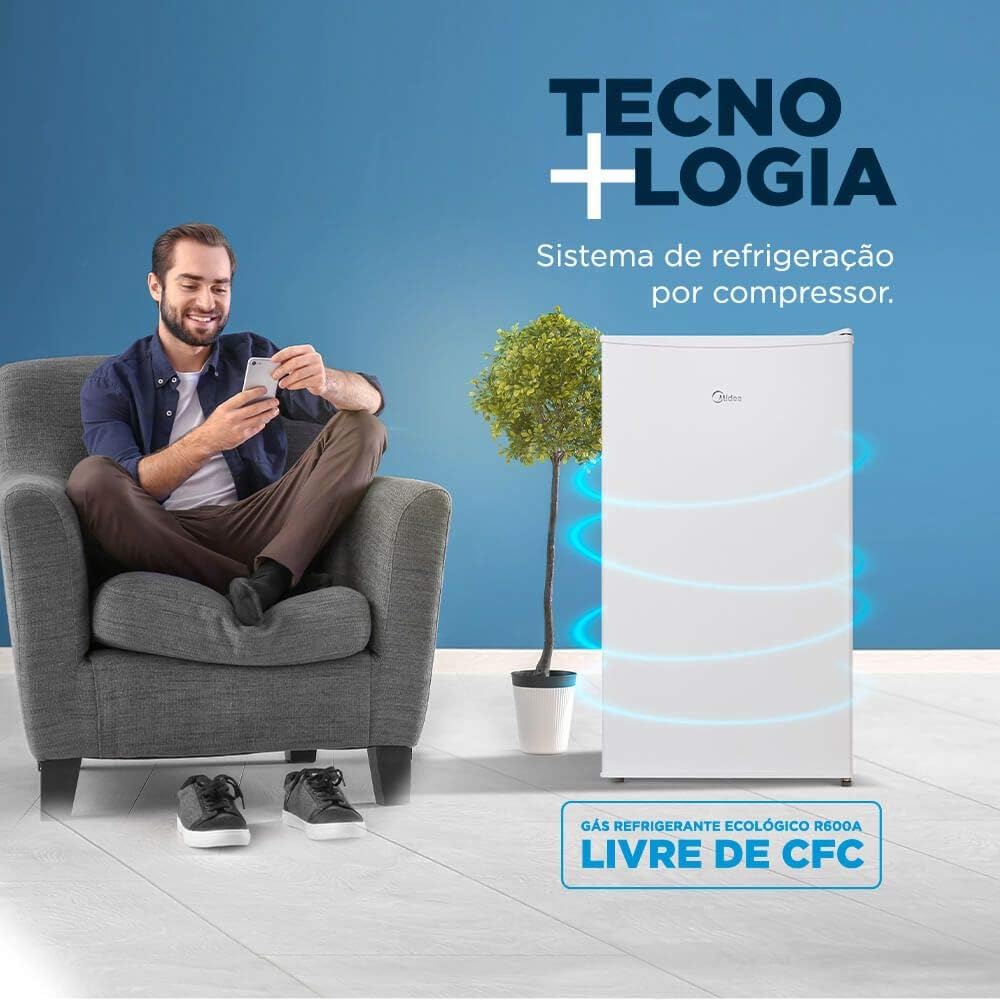 Homem sentado ao lado do frigobar Midea branco com destaque para tecnologia e sistema de refrigeração ecológico